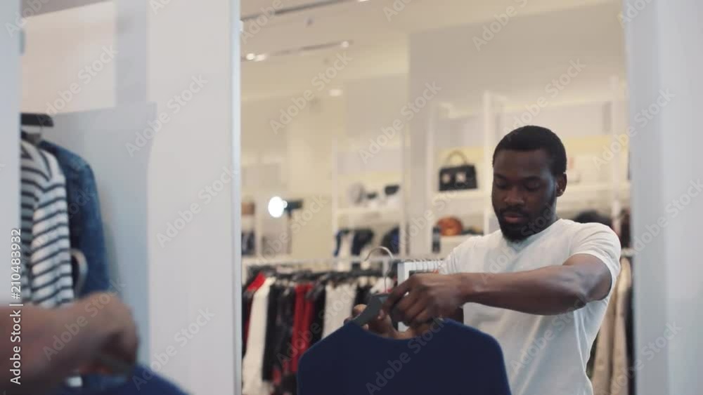 Attractive african american man chooses sweater looking in the mirror in store mall design business fashion face shopping beauty, black clothing beautiful casual model style close-up Attractive african american man chooses sweater looking in the mirror in store mall design business fashion face shopping beauty, black clothing beautiful casual model style close-up