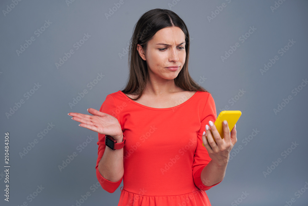 Unpleasant content. Dark-haired young woman reading a text message from her phone and being displeased with its content Unpleasant content. Dark-haired young woman reading a text message from her phone and being displeased with its content