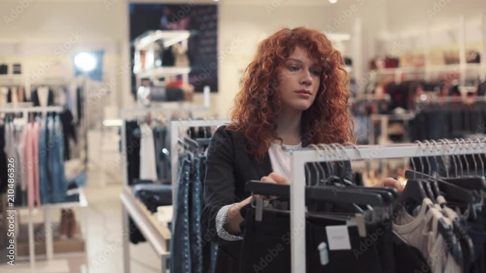 young woman with curly red hair choose clothes at store hold smile design shopping girl beautiful attractive shop cute happy pretty style curly hair portrait serious close up slow motion