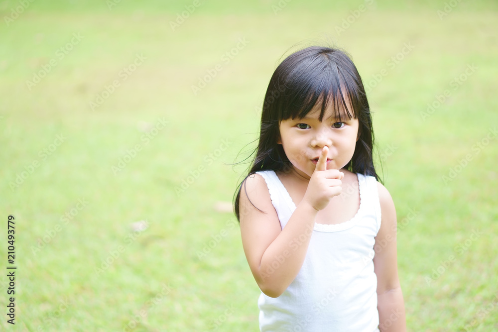 Asian children cute or kid girl squat and forefinger close mouth for tell quietly with silent and surprise or play hide and seek with green grass meadow space Asian children cute or kid girl squat and forefinger close mouth for tell quietly with silent and surprise or play hide and seek with green grass meadow space
