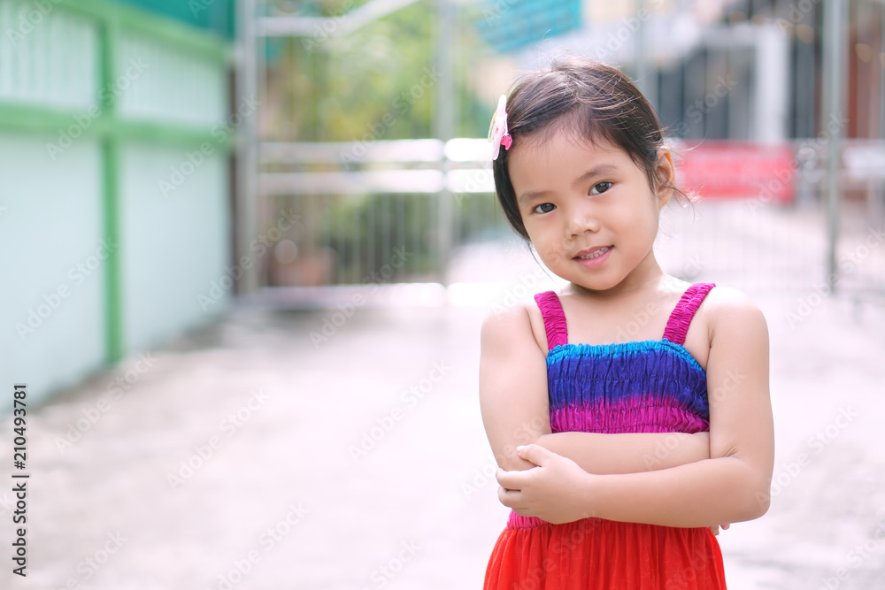 Asian children cute or kid girl smile with cross one's arm stand and wear colorful dress at home or street and city for confident or excitement and fashion with space