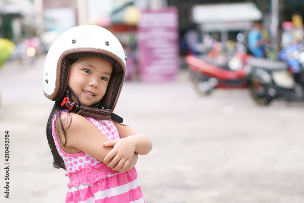 Asian children cute or kid girl smile wear classic white motorcycle or bike helmet with cross one's arm for confident and head safety or protect on street and road riding or driver travel with space Asian children cute or kid girl smile wear classic white motorcycle or bike helmet with cross one's arm for confident and head safety or protect on street and road riding or driver travel with space