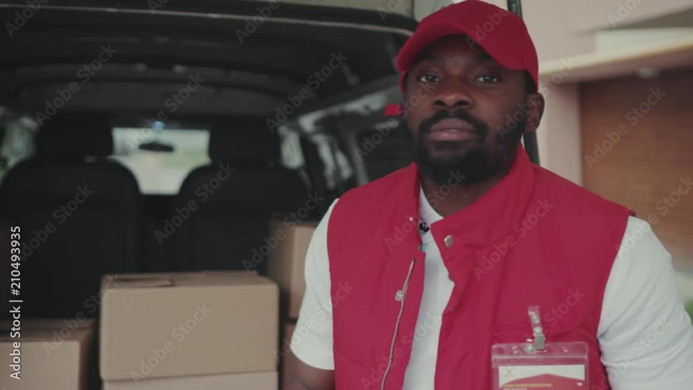 Close up face handsome courier young african american man look at camera smile portrait delivery postal uniform job worker cardboard post commercial distribution transport box package logistic service