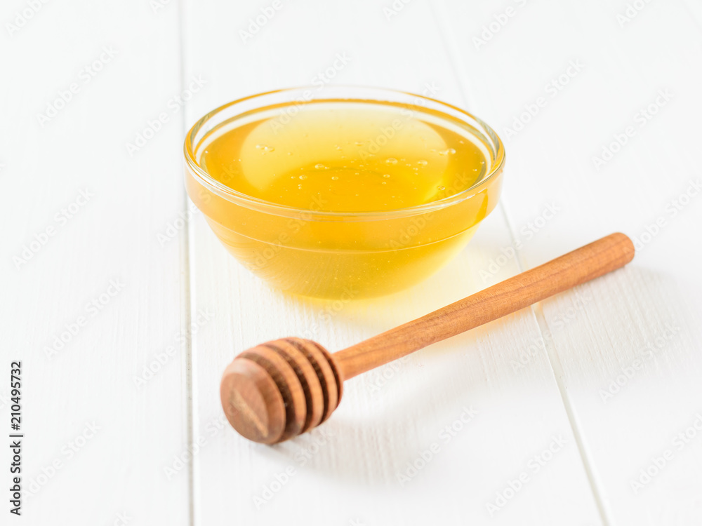 A bowl of honey and a wooden honey spoon on a white wooden table. A bowl of honey and a wooden honey spoon on a white wooden table.