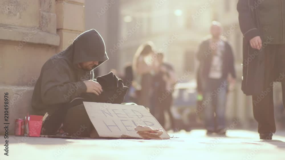 Close up homeless man sitting on street with sign need help people walk around honeliness sad social cardboard homeless beggar face poverty poor hungry dirty unemployed despair slow motion portrait