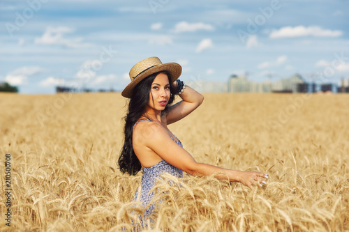 Young romantic woman in light summer dress on a walk in the wheat field