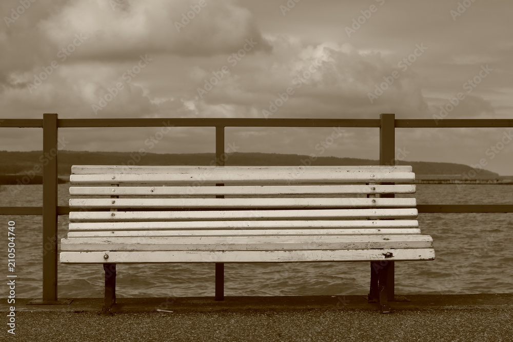 Pusta drewanian ławka na molo, w tle morze (jezioro), linia brzegowa, pochmurne niebo, sepia Pusta drewanian ławka na molo, w tle morze (jezioro), linia brzegowa, pochmurne niebo, sepia
