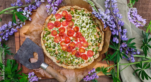 Aspargus cherry tomato pie on the table for summer festivites. Decorated with blue lupines. Flat lay and top view for quice photo