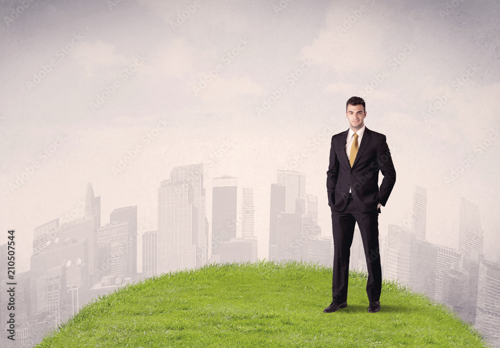A confident male well looking office manager standing in small green grass in front of city landscape with tall buildings concept. A confident male well looking office manager standing in small green grass in front of city landscape with tall buildings concept.