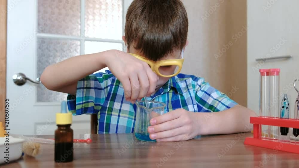 Experiments on chemistry at home. Boy mixes the blue liquid and powder in the beaker with glass stick. Experiments on chemistry at home. Boy mixes the blue liquid and powder in the beaker with glass stick.