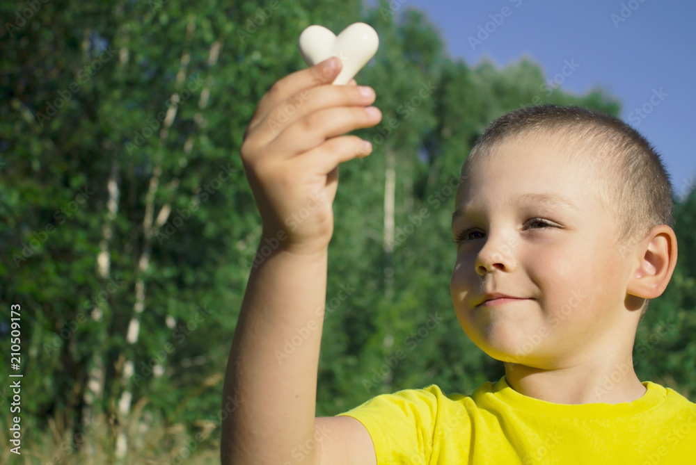the boy in a yellow shirt holds a heart in his hands against the background of nature. the boy in a yellow shirt holds a heart in his hands against the background of nature.