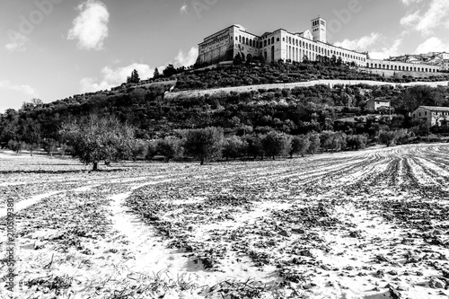 View of Assisi town (Umbria) in winter, with a field covered by snow and sky with white clouds © Massimo