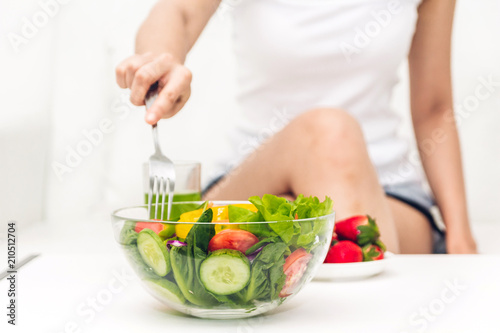 Woman eating healthy fresh salad in a bowl on sofa at home.dieting concept.healthy lifestyle with green food