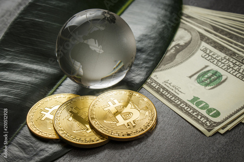 Three gold coins in the form of bitcoin on a table with banknotes and a glass globe