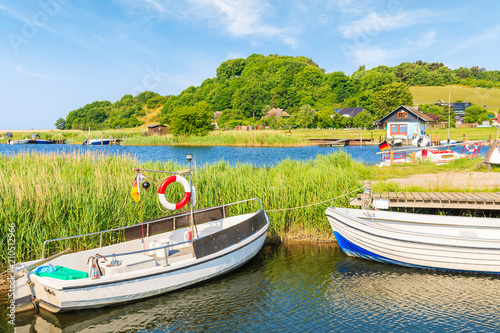 Fishing boats mooring in Baabe port and view of Moritzdorf village with houses on lake shore, Ruegen island, Baltic Sea, Germany