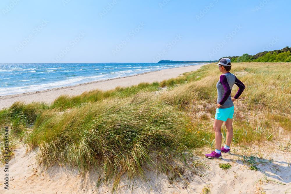 Young woman tourist standing on beach with grass sand dunes in Lobbe village, Ruegen island, Baltic Sea, Germany
