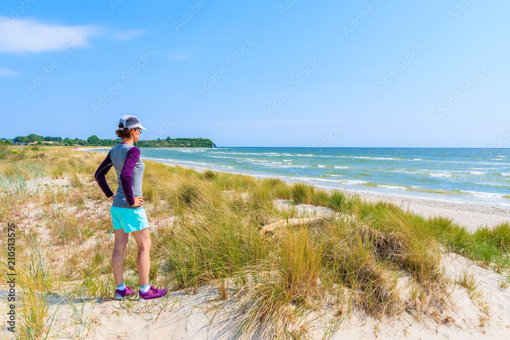 Young woman tourist standing on beach with grass sand dunes in Lobbe village, Ruegen island, Baltic Sea, Germany