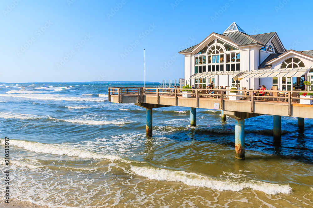 Obraz premium SELLIN, RUEGEN ISLAND - MAY 31, 2018: Pier with historic building on sandy beach in Ostseebad Sellin on Baltic Sea coast, Germany. Ruegen is popular tourist destination because of its architecture.