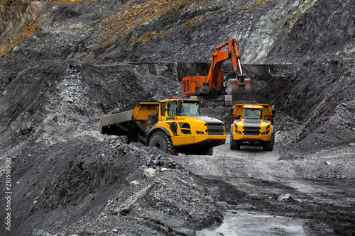 Excavator in an open coal mine. Heavy industry. Two quarry dump trucks.