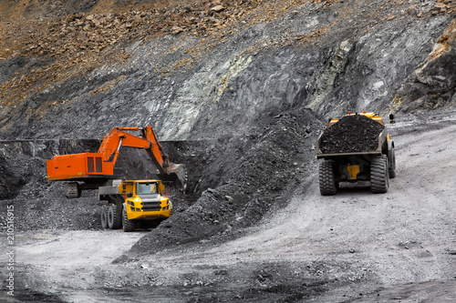 Excavator in an open coal mine. Heavy industry. Two quarry dump trucks.