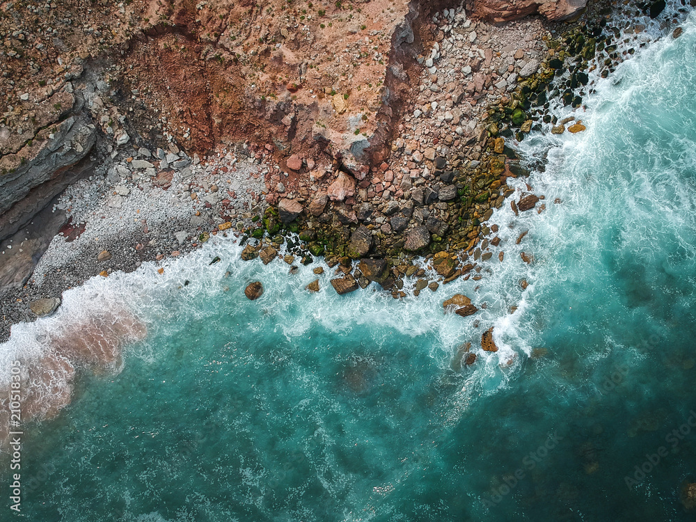 Naklejka premium Aerial top view of sea waves hitting rocks on the beach with turquoise sea water. Amazing rock cliff seascape in the Portuguese coastline.
