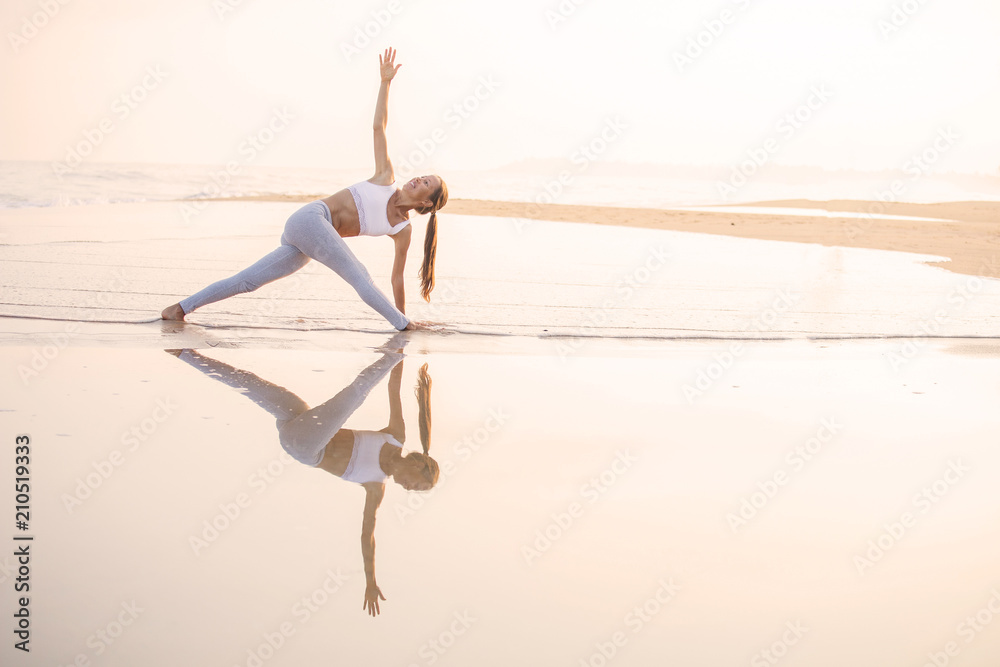 Fototapeta premium Caucasian woman practicing yoga at seashore of tropic ocean