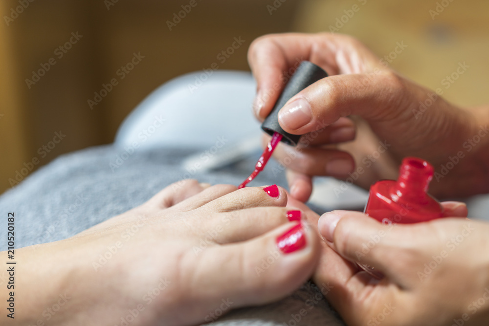 The master covers the customer's nails with varnish. Hands in gloves cares about a woman's foot nails. Pedicure, manicure beauty salon concept. Nail varnishing in red color. The master covers the customer's nails with varnish. Hands in gloves cares about a woman's foot nails. Pedicure, manicure beauty salon concept. Nail varnishing in red color.