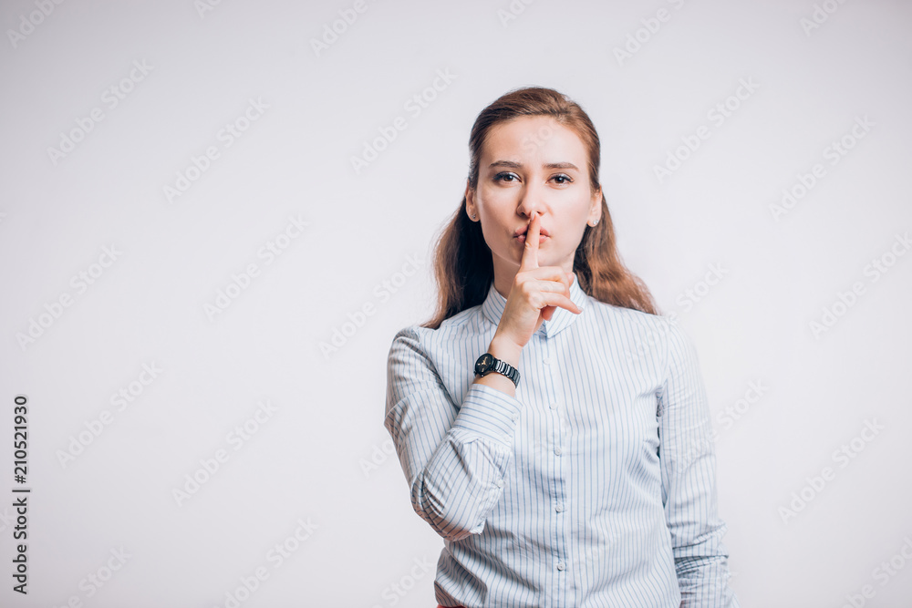 Beautiful young brunette woman keeps forefinger on lips, tells secret , demands silence on a white background Beautiful young brunette woman keeps forefinger on lips, tells secret , demands silence on a white background