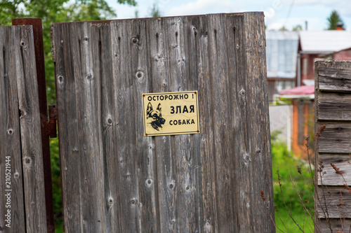  the inscription in Russian: carefully angry dog. plaque on a wooden fence