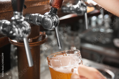Bartender pouring beer from tap into glass in bar, closeup © New Africa