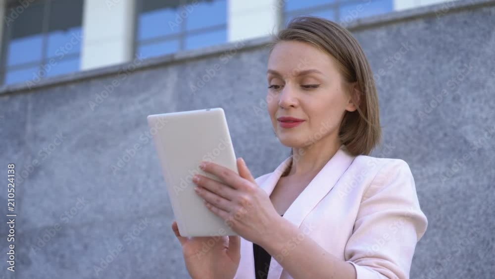 A woman is working on a tablet on the street. on the background of an office building. Attractive middle-aged woman in a jacket. 4K A woman is working on a tablet on the street. on the background of an office building. Attractive middle-aged woman in a jacket. 4K