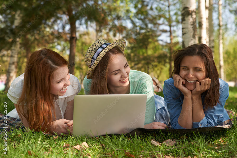 group of young teen girls are lying on a summer green lawn with a laptop and laughing. The concept of outdoor recreation, warm weather and pleasant holidays group of young teen girls are lying on a summer green lawn with a laptop and laughing. The concept of outdoor recreation, warm weather and pleasant holidays