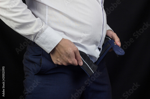 A fat young man in a white shirt with a big belly can not fasten his pants, close-up