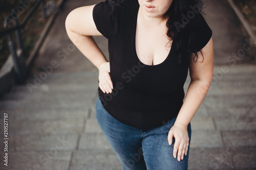 Overweight woman suffering from breathe shortness stepping on stairs. Excess weight, heart problems, health care and medical concept photo