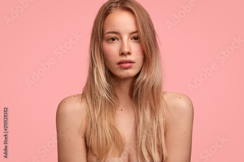 Cropped shot of calm beautiful naked female with long hair, demonstrates healthy skin, poses for fashion magazine, has serious expression, isolated on pink background. People, beauty, lifestyle