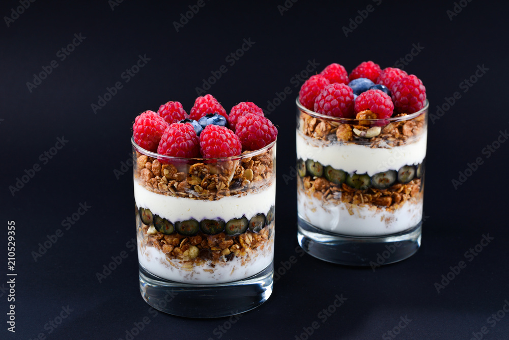 Healthy blueberry and raspberry parfait in a glass on a black background. Two portions. Space for text or design. Healthy blueberry and raspberry parfait in a glass on a black background. Two portions. Space for text or design.