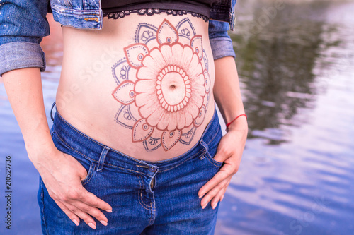 woman on a background of water in jeans clothes and mehendi on her stomach. background lake, river photo