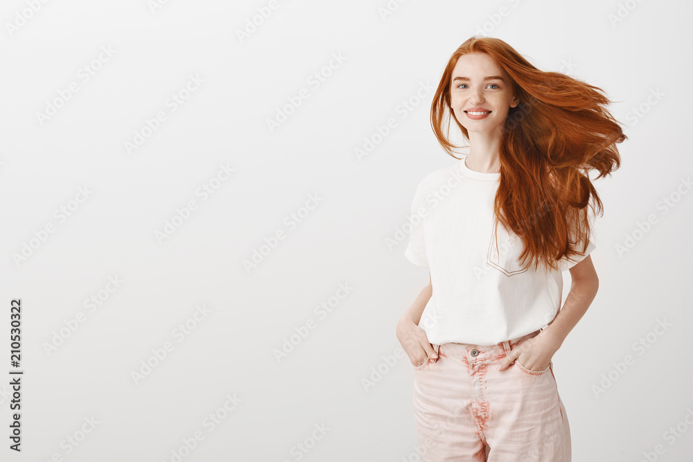 Studio shot of attractive confident and happy redhead woman with long natural hair, holding hands in pockets, smiling broadly at camera, walking along beach and enjoying evening near seaside Studio shot of attractive confident and happy redhead woman with long natural hair, holding hands in pockets, smiling broadly at camera, walking along beach and enjoying evening near seaside