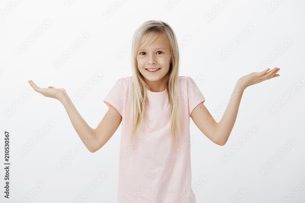 Girl hide moms phone, imitating she has no clue what it happening. Portrait of adorable young european girl with blonde hair, shrugging with raised spread palms, smiling broadly, clueless and unaware Girl hide moms phone, imitating she has no clue what it happening. Portrait of adorable young european girl with blonde hair, shrugging with raised spread palms, smiling broadly, clueless and unaware