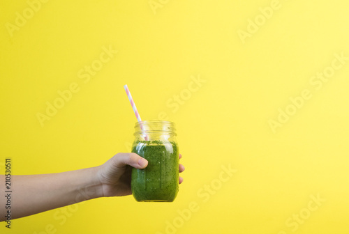 Woman hand holding smoothie shake against colored wall. Drinking green healthy smoothie concept.