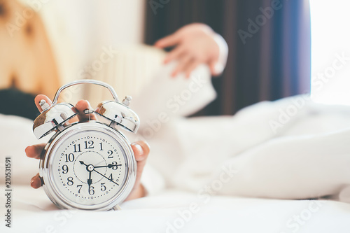 Irritated young woman putting her alarm clock off in the morning with soft morning light. Relaxing concept.