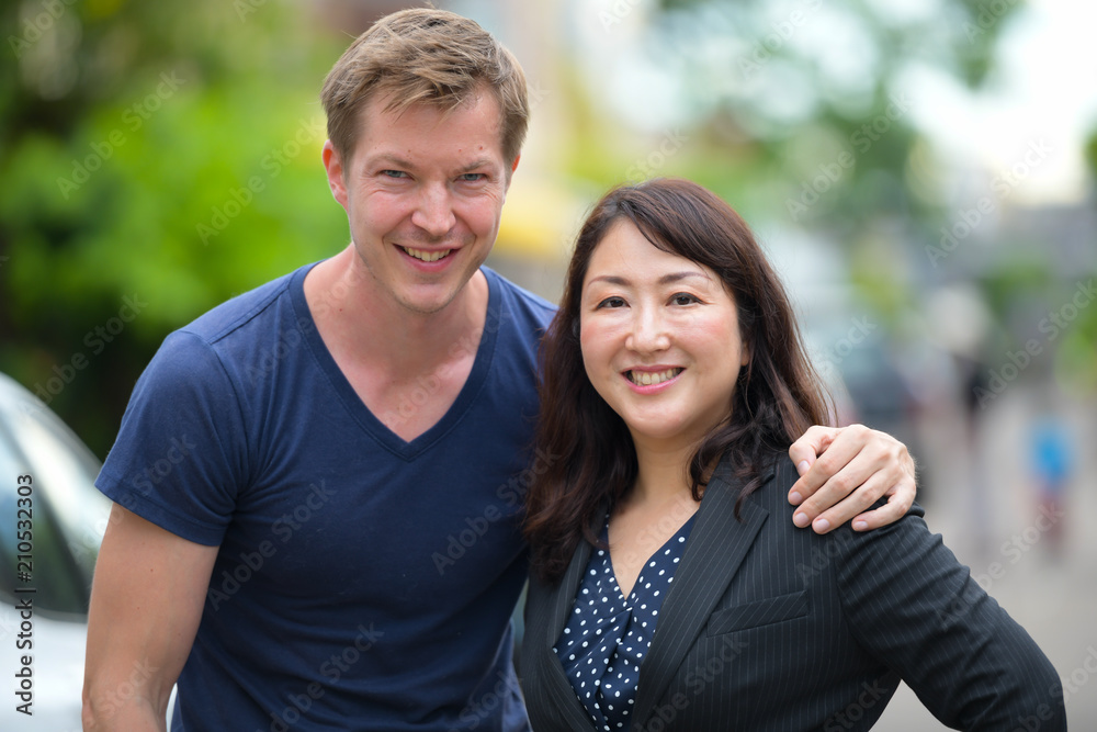 Mature beautiful Asian businesswoman and young Scandinavian man together in the streets outdoors Mature beautiful Asian businesswoman and young Scandinavian man together in the streets outdoors