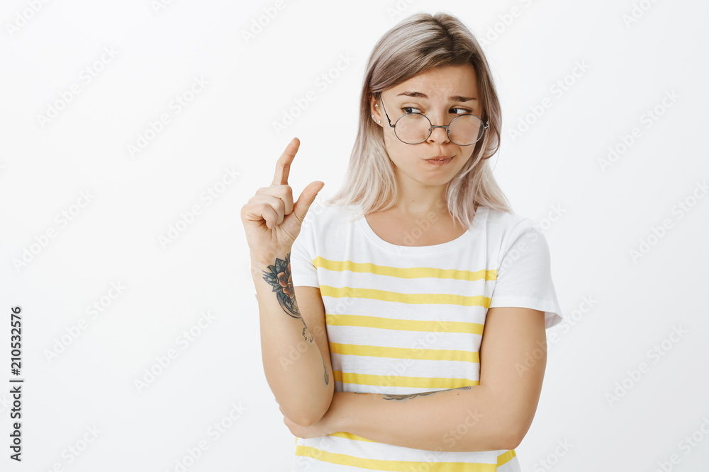 Not sure if this size fits. Unsure doubtful cute european female student with fair hair and tattoos in round glasses and trendy t-shirt, shaping something small or tiny with hand and peeking Not sure if this size fits. Unsure doubtful cute european female student with fair hair and tattoos in round glasses and trendy t-shirt, shaping something small or tiny with hand and peeking