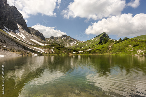 Crystal clear water of alpine lake Lache in Tannheimer high valley with mountain refuge Landsberger Hut in the background  Tyrol  Austria