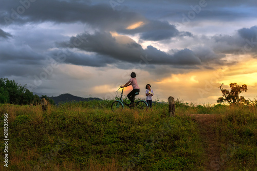 Two children playing paper airplane and ride bicycle on mountain at sunset