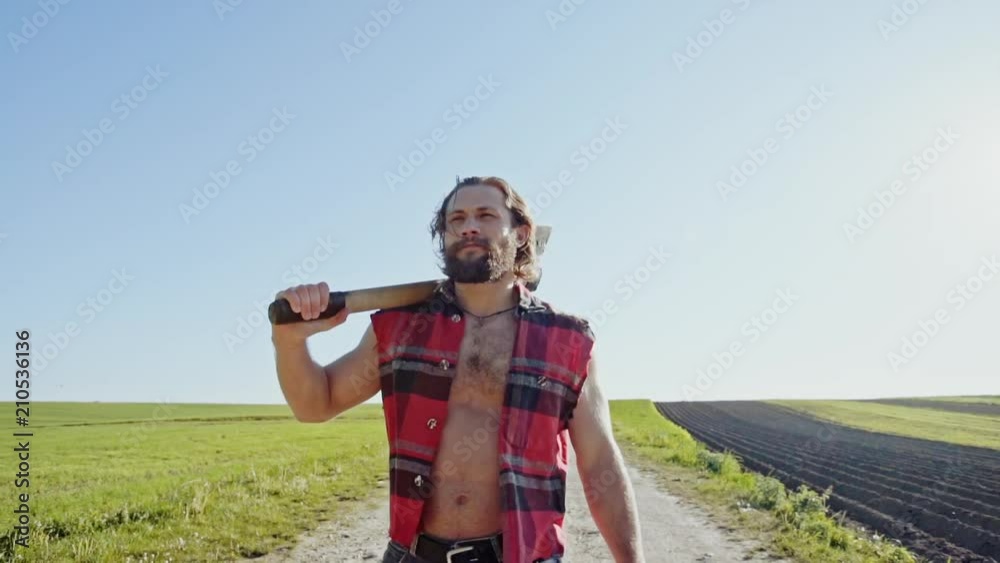 Lumberjack worker walking in the farmland on a sunny, warm summer day Lumberjack worker walking in the farmland on a sunny, warm summer day