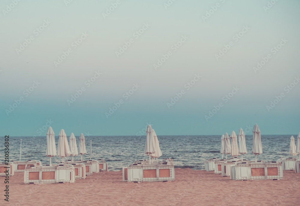 Fototapeta premium Beach with closed umbrellas and sunbeds in the evening. Toned.
