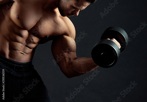 Frontview of strong bodybuilder with clear muscular relief lifting heavy dumbbell in gym. Sport lifestyle. Regular gym trainings. Fit sporty body. Lifestyle. Looking healthy and sexy. Working hard.