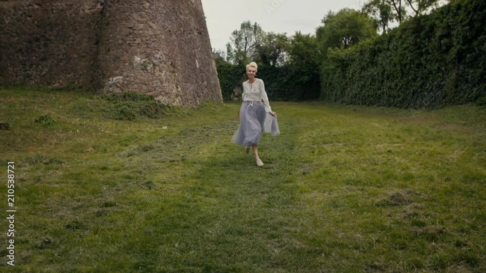 Young happy smiling woman wearing tutu skirt, white blouse, straw gat, running to camera, whirling around herself Young happy smiling woman wearing tutu skirt, white blouse, straw gat, running to camera, whirling around herself