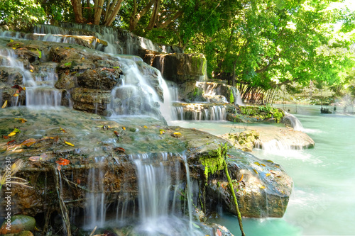 Low speed shutter or long exposure of waterfall on big rock under green tree in a forest with beautiful turquoise color of water